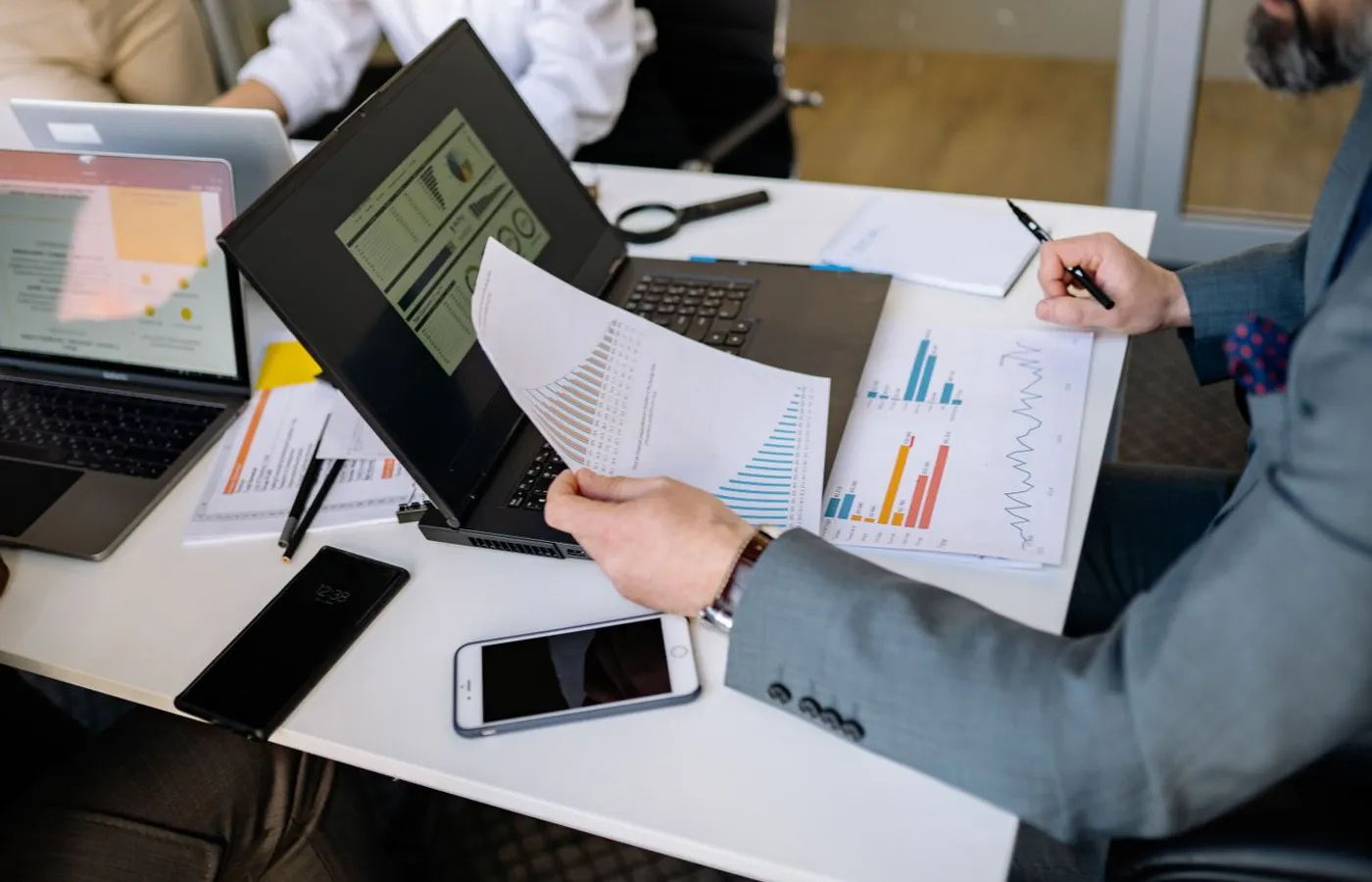 Professionals analyzing charts and data on laptops during a business meeting.